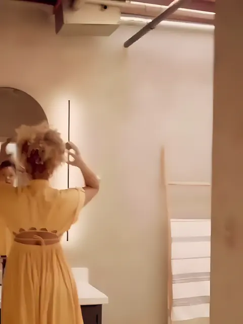 A woman in mustard linen at the arched, backlit mirror of the Hair Club